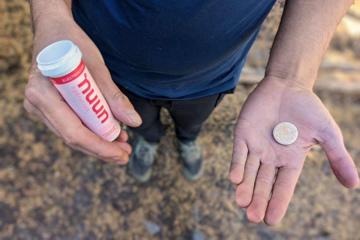 A hiker holding a tube of Nuun in one hand and a Nuun tablet in the other